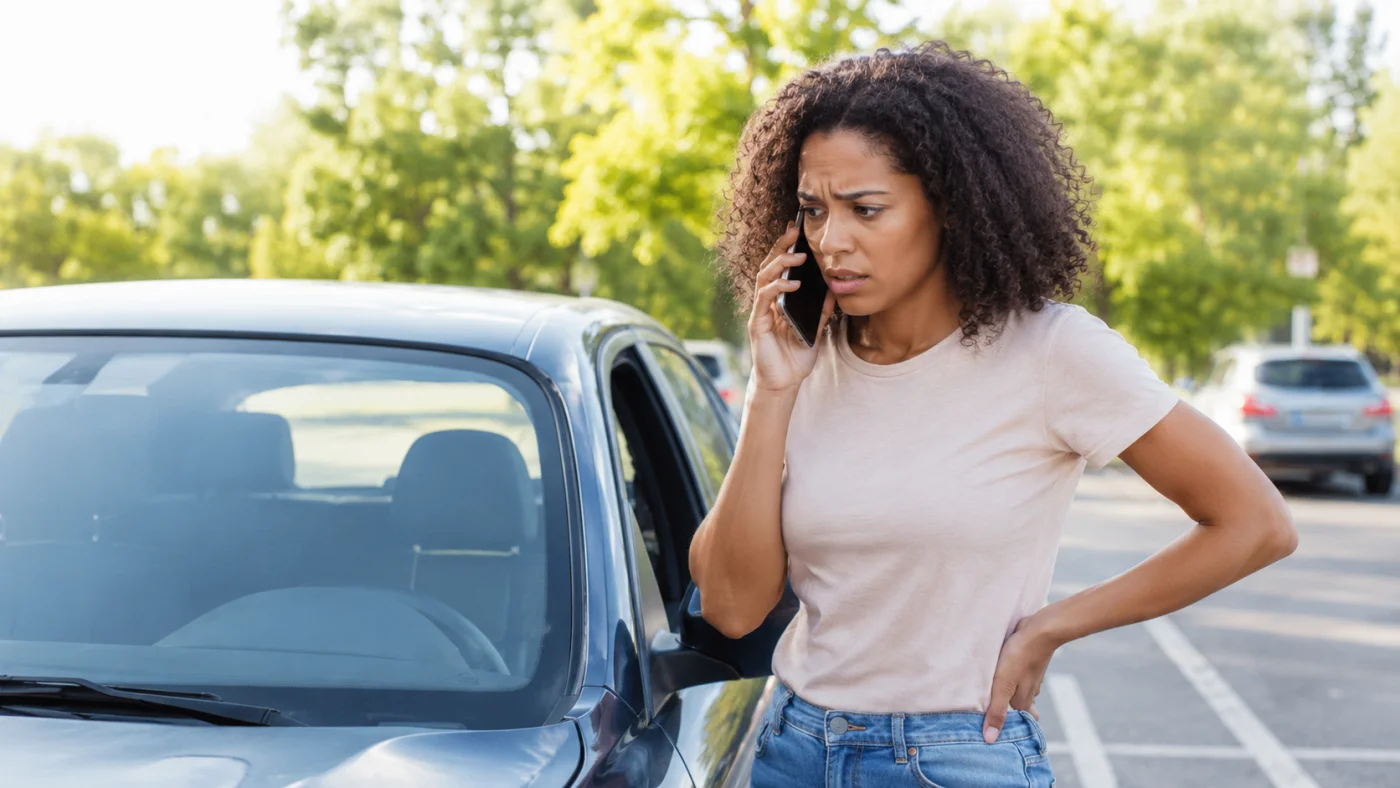Personne au téléphone à côté d'une voiture garée, en train d'appeler les secours